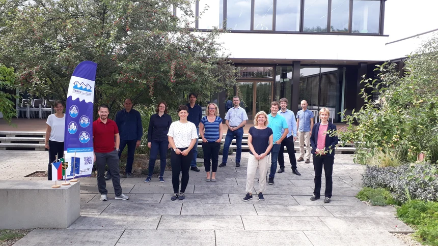 Skupinové foto účastníků jednání projektových partnerů STRIMA II pořízené za dodržování odstupů v atriu budovy IÖR. V popředí je vidět i muší křídlo s logem projektu STRIMA II.