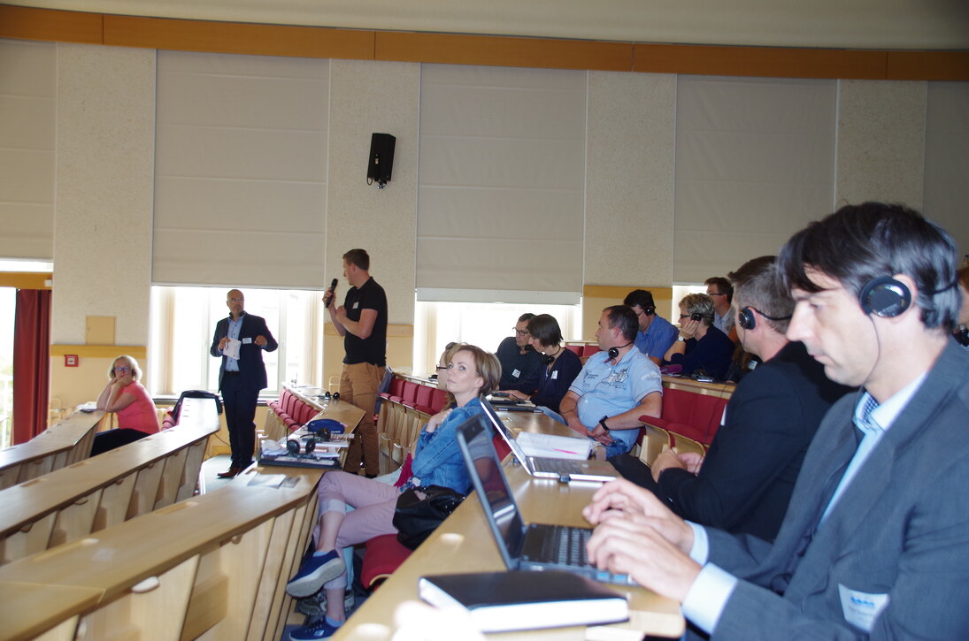 Das Foto zeigt den Blick in die Hörsaalreihen während einer Diskussionsrunde. Der Moderator der Veranstaltung Herr Dr. Peter Heiland steht bei einem fragenden Forumsteilnehmer zur Mikrofonübergabe. 